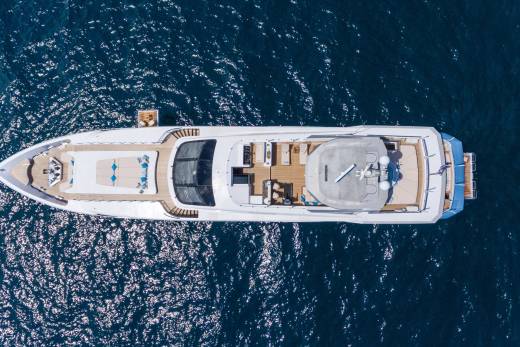 A luxurious yacht glides across the sparkling blue ocean, its decks adorned with comfortable seating and sun loungers.