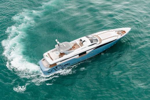 A sleek blue and white yacht glides through turquoise waters, leaving a foamy wake in its path.