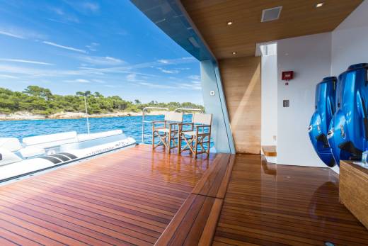 Relax on the teak deck of a luxury yacht, surrounded by the azure waters and lush green coastline.