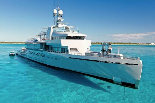 A luxurious superyacht glides through crystal-clear turquoise waters under a bright blue sky.