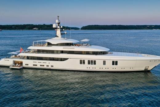 A luxurious white superyacht glides serenely on calm blue waters under a twilight sky.