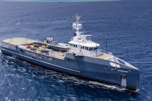 A sleek grey vessel with a helipad and tenders cruises through the deep blue ocean.