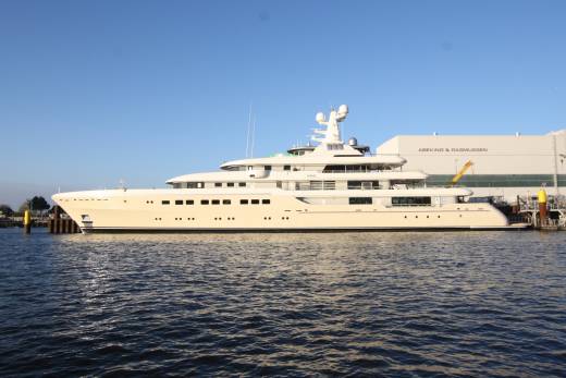 A magnificent superyacht is docked alongside a shipyard under a clear blue sky.