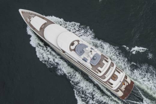 A luxurious white yacht cruises through dark, choppy waters, leaving a foamy wake in its path.