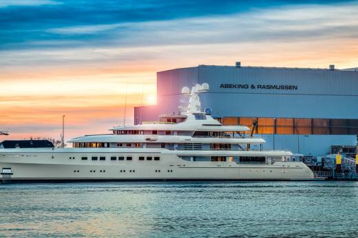 A luxurious superyacht docks at the Abeking & Rasmussen shipyard during a vibrant sunset.