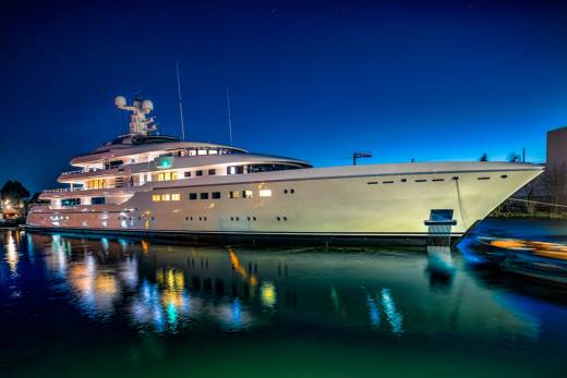 A luxurious yacht gleams under the night sky, its lights reflecting on the tranquil water.