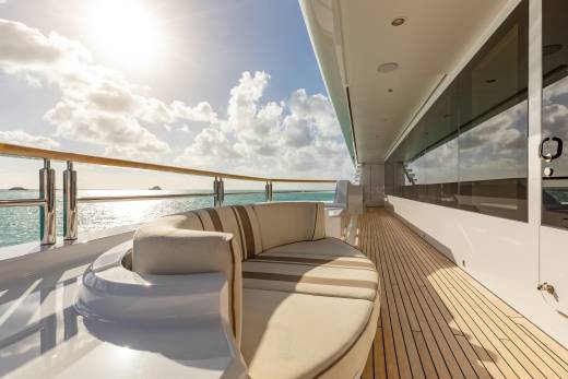 Sunlight glints off the turquoise sea as a plush, striped sofa awaits relaxation on this luxurious yacht deck.