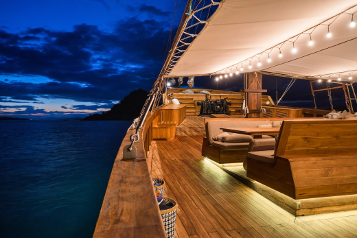 Warm lights illuminate the wooden deck of a luxurious yacht as dusk settles over the tranquil sea.
