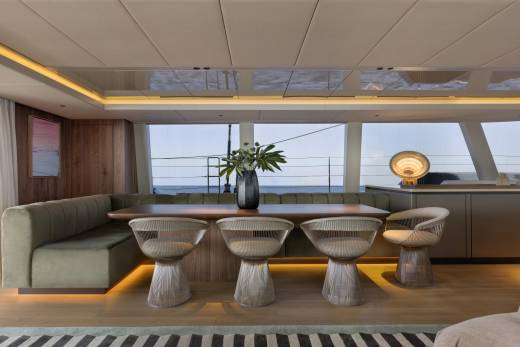 A sleek dining area on a yacht features a plush banquette, modern chairs, and a large window overlooking the ocean.