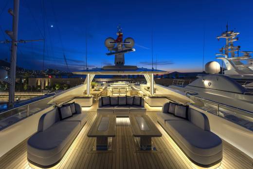 Luxurious yacht deck seating is illuminated at dusk with a backdrop of a crescent moon and distant city lights.