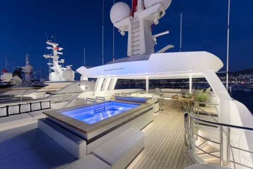 The illuminated pool on this luxurious yacht deck offers a serene evening dip with a backdrop of a bustling harbor.