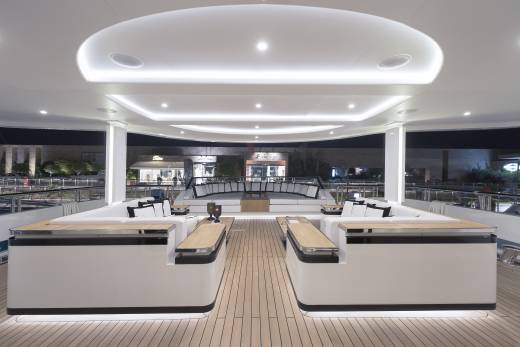 Luxurious white seating and sleek wooden accents create a modern lounge area on the deck of a yacht at night.