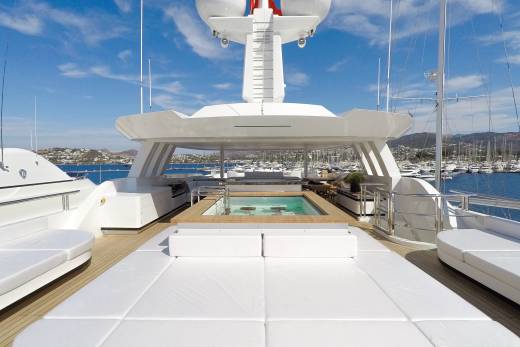 Relax in the onboard jacuzzi surrounded by plush white loungers and a picturesque marina view.