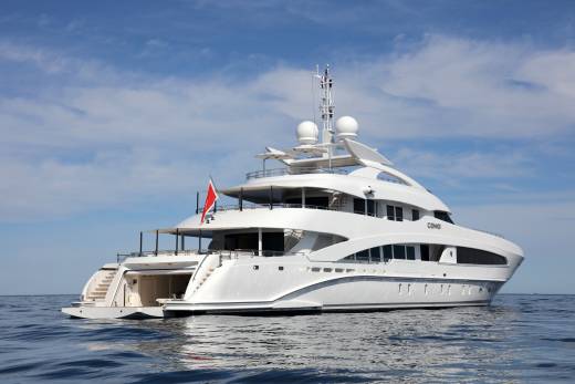 A luxurious white yacht named COMO glides serenely across the calm blue ocean under a bright, cloudy sky.