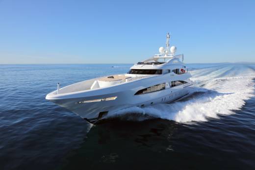 A sleek white superyacht glides through the deep blue ocean, leaving a foamy white wake under a clear sky.