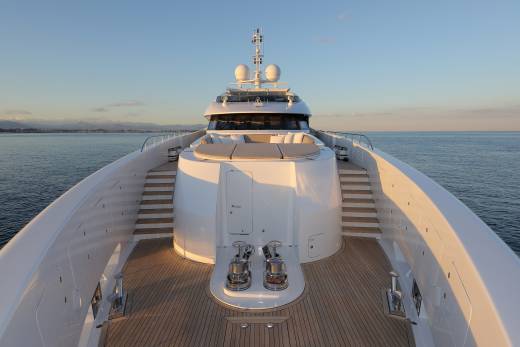 The sun casts a warm glow on the pristine deck of a luxurious yacht as it glides across the calm, blue sea.