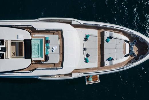 An aerial view reveals a luxurious yacht with a sparkling pool and ample sun loungers floating on the deep blue sea.