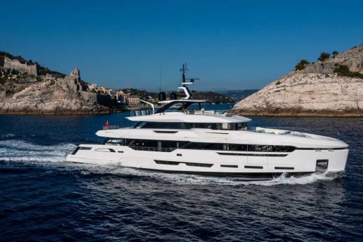 A sleek white superyacht glides through the deep blue sea past a historic Italian coastline.