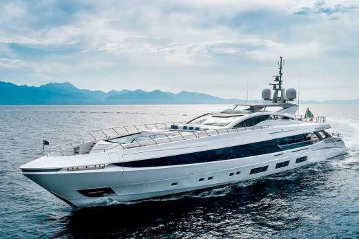 A sleek white yacht cuts through the deep blue ocean with a mountainous coastline in the distance.