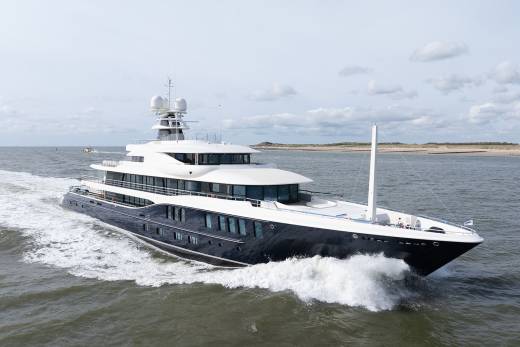 A sleek, dark-hulled superyacht cuts through choppy waters under a cloudy sky.