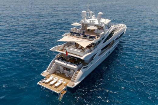 A luxurious white yacht with multiple decks and lounge areas glides across the deep blue sea.