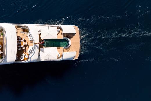 A luxurious yacht glides through deep blue waters, its deck featuring a pristine pool and elegant seating areas.