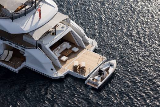 A luxurious yacht with an open deck and a tender boat docked alongside floats on the shimmering blue sea.