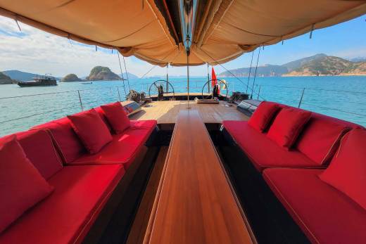Luxurious red cushions invite relaxation on the deck of this elegant yacht, cruising through turquoise waters amidst scenic islands.