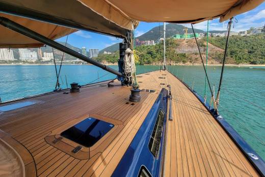 The sun-drenched deck of a luxurious yacht offers a serene vantage point of a tranquil bay dotted with distant cityscapes.