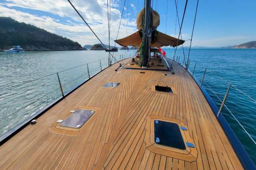 The polished wooden deck of a sailboat stretches towards the horizon under a bright blue sky dotted with clouds.