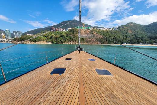 Sailing on turquoise waters towards a lush green coastline dotted with modern buildings under a clear blue sky.