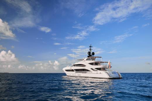 A luxurious white yacht glides across the deep blue ocean under a vast sky dotted with clouds.