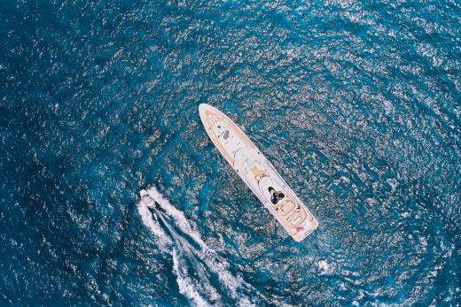 A luxurious yacht glides through the sparkling blue ocean, leaving a foamy wake behind it.