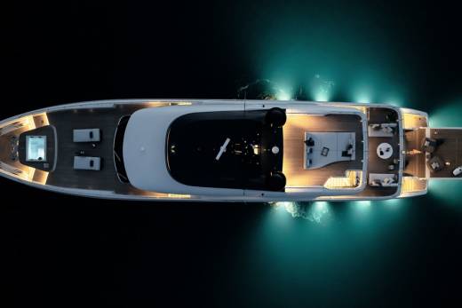 An aerial view captures a luxurious yacht illuminated by underwater lights, showcasing its sleek design and inviting deck spaces.