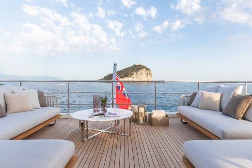 Relax on the spacious deck of a luxury yacht, enjoying the serene ocean views and a picturesque island in the distance.