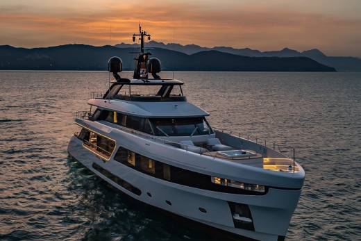 A luxurious yacht glides across calm waters at sunset, with silhouetted mountains in the distance.