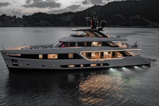 A luxurious yacht named Legend glides through calm waters at dusk, its interior lights casting a warm glow.