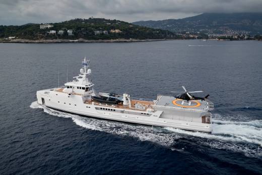 A sleek white yacht cruises through the deep blue sea, its helideck ready for a waiting helicopter.