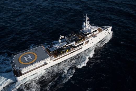 A sleek white superyacht cruises through dark, choppy waters, its helipad clearly visible at the stern.