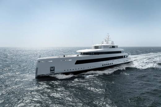 A sleek white superyacht cuts through the choppy blue sea under a clear sky.