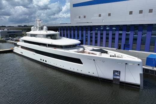 A sleek white superyacht is docked beside a modern industrial building with blue accents.