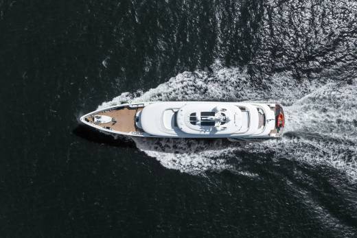 A sleek white yacht cuts through dark, rippling water, leaving a foamy white wake in its path.