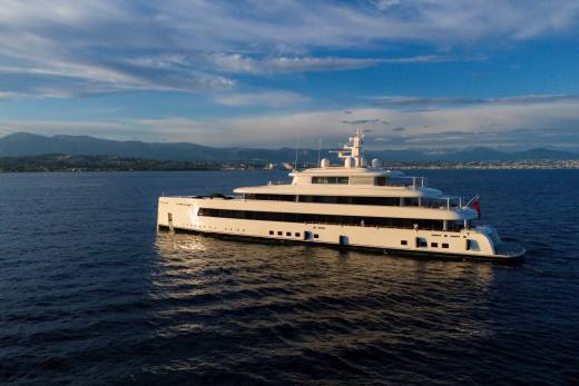 A luxurious white yacht glides across the deep blue sea under a dramatic sky with distant mountains on the horizon.