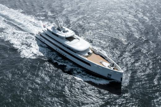 A sleek white superyacht glides through the choppy, sun-dappled ocean, leaving a foamy wake.