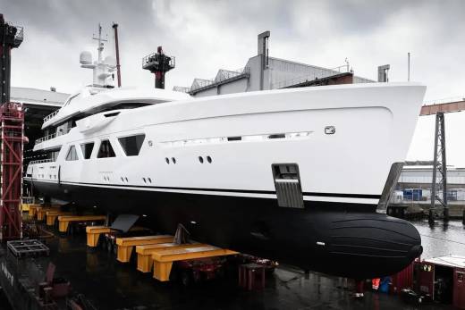 A magnificent white and black yacht rests on yellow cradles in a dry dock, awaiting its launch into the water.