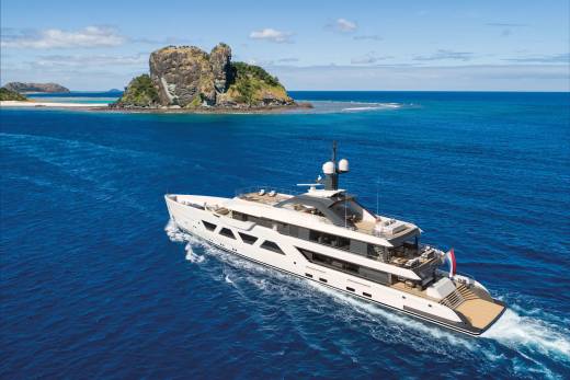 A luxurious white yacht cruises through the vibrant blue ocean near a rocky, verdant island.