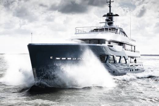A large, sleek yacht cutting through the choppy waves, with a dramatic cloudy sky in the background.