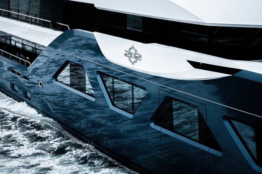 A large, sleek white yacht with a distinctive logo on its side, cutting through the choppy blue waters in the background.