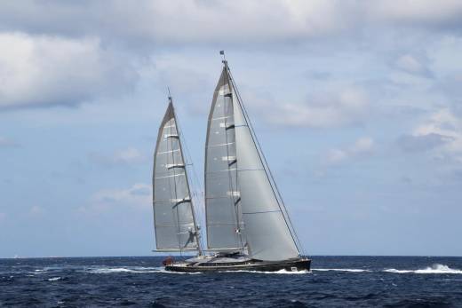 A sleek, modern sailing yacht cuts through the deep blue ocean under a cloudy sky.