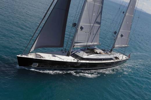 A sleek black yacht glides through turquoise waters under full sail, its modern design contrasting with the timeless beauty of the sea.